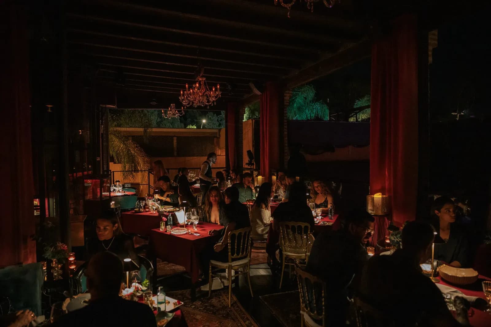 Dimly lit dining room at LØV Marbella with red curtains and laid tables