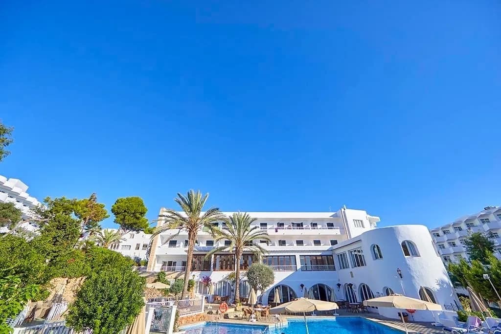 White facade of Costa del Sur hotel in Cala d'Or with pool and palm trees
