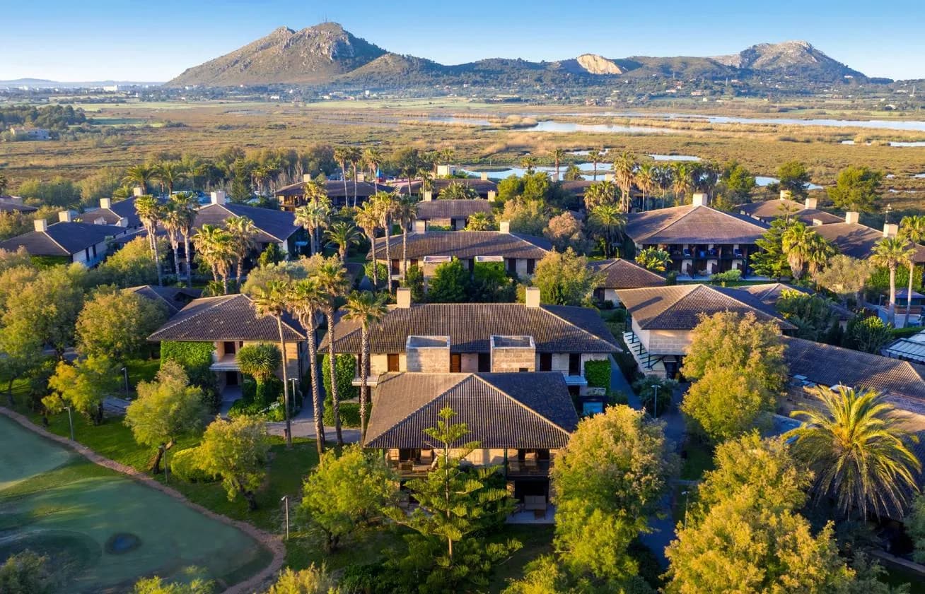 Aerial view of PortBlue Club Pollentia Resort & Spa with villas, palm trees and a mountain