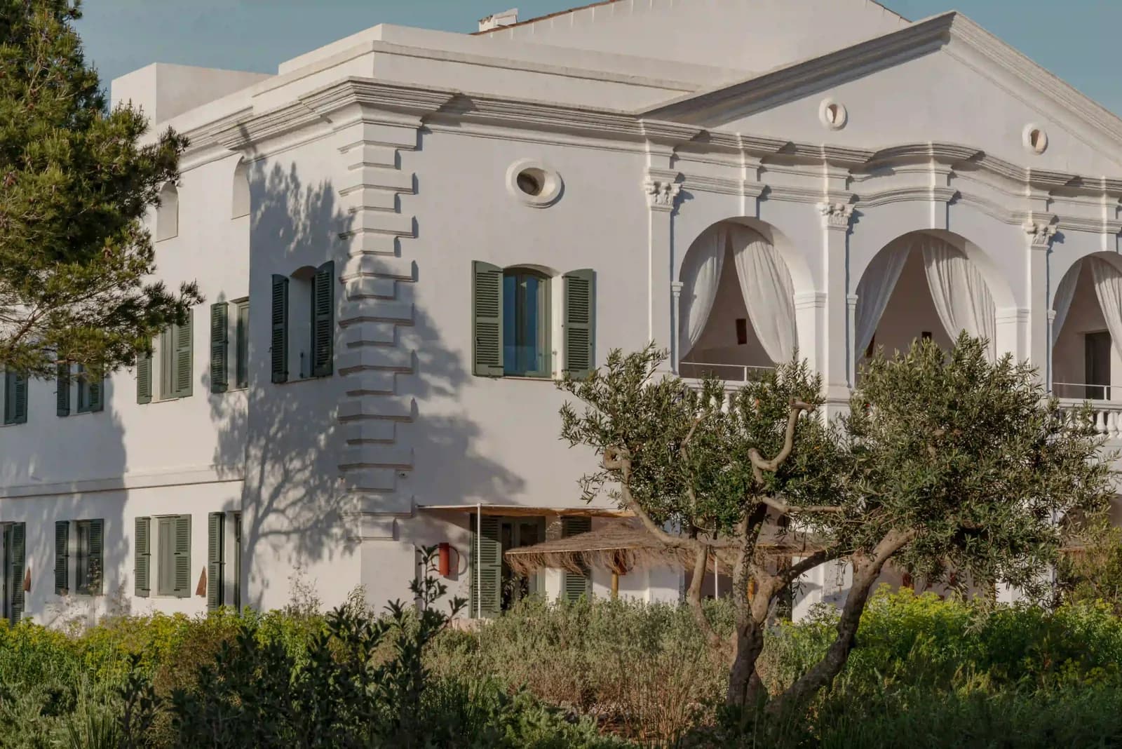White facade of Menorca Experimental hotel framed by olive trees in Menorca