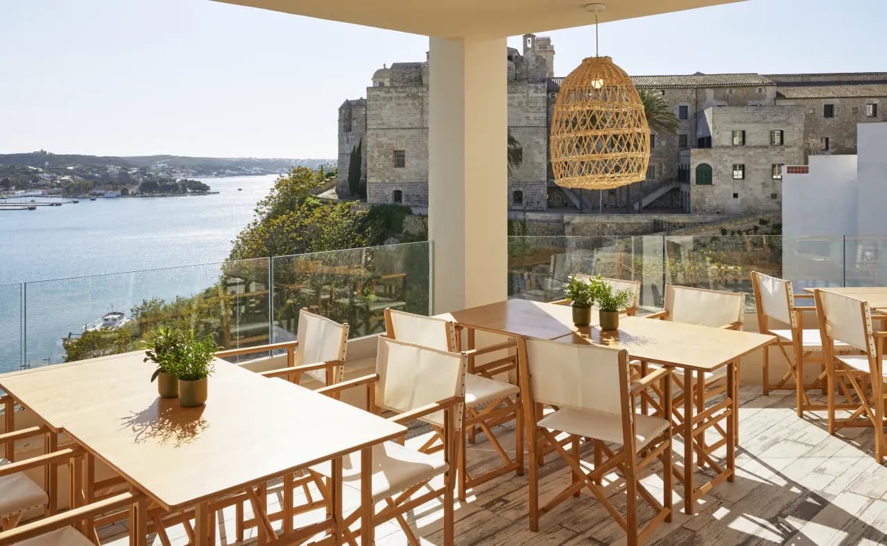 Shaded terrace with wooden tables and harbour view in Maó, Menorca