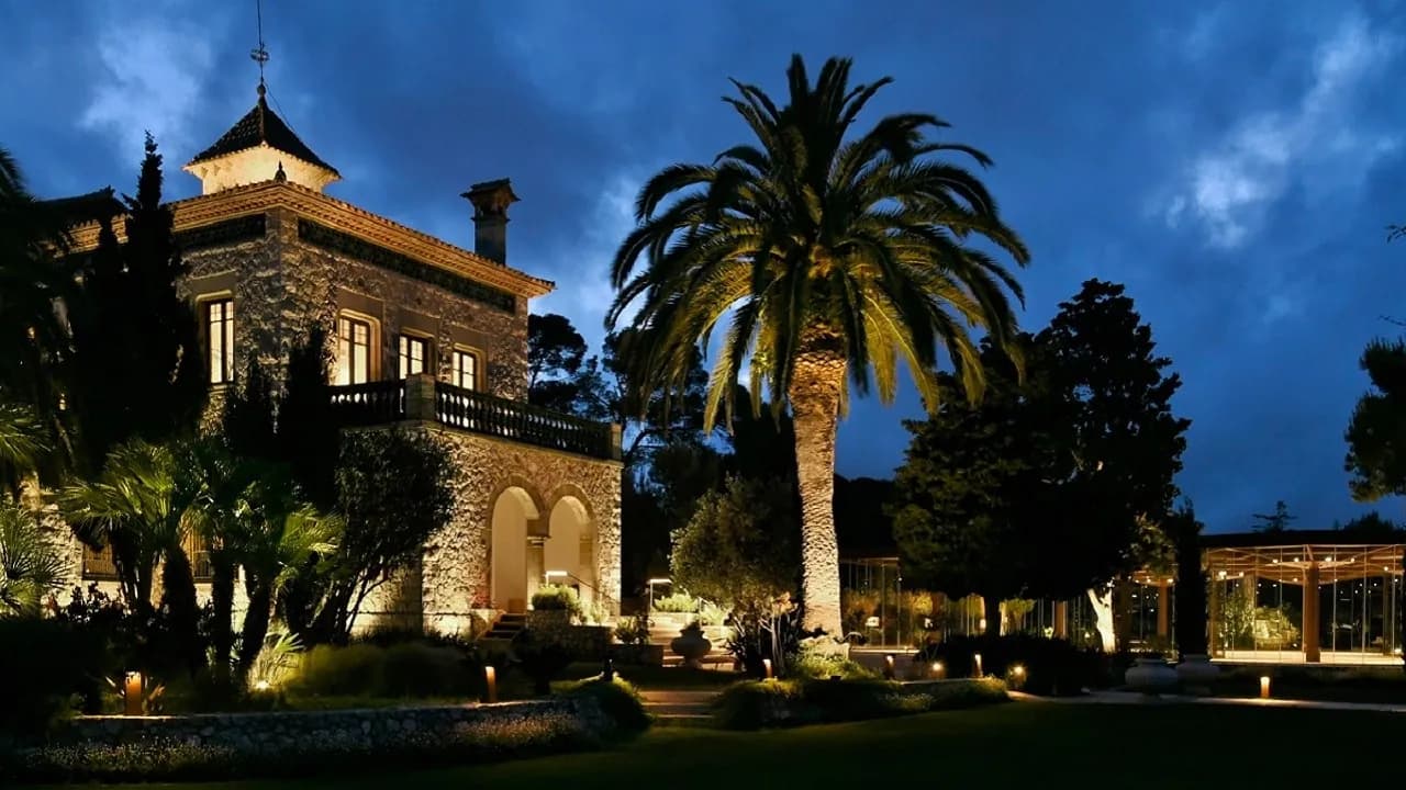 Facade of Xalet del Nin at dusk, palm tree and gardens near Barcelona