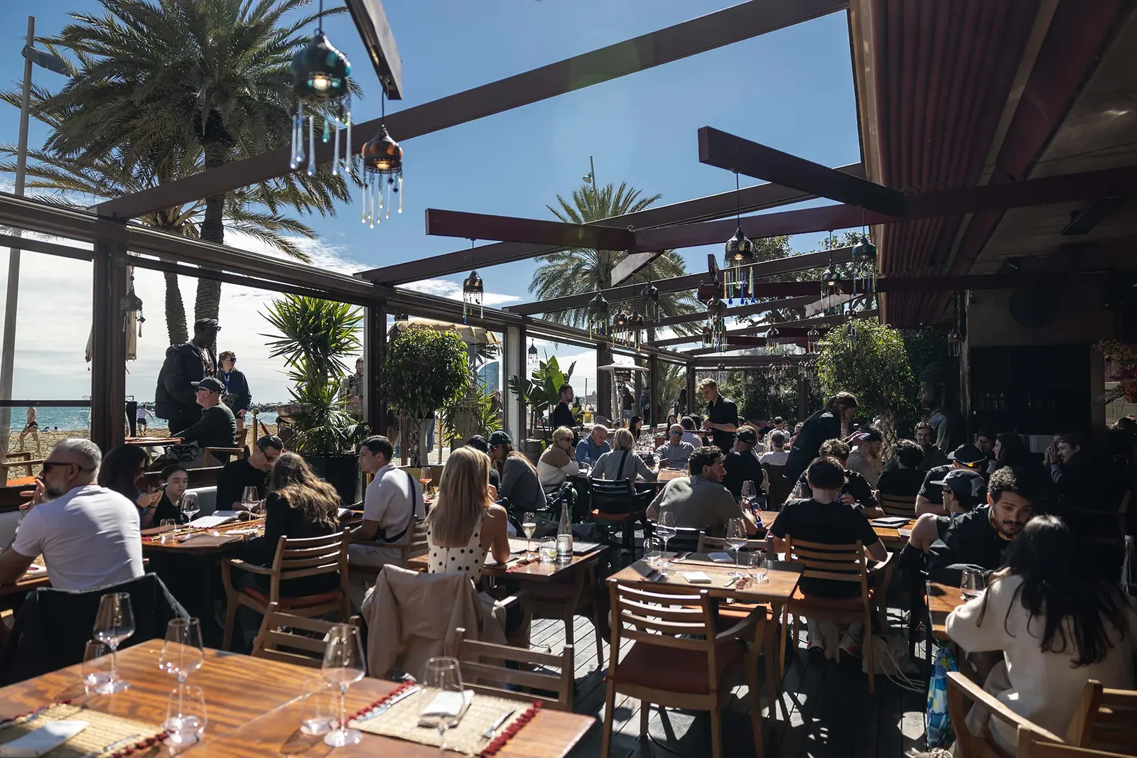 Shaded terrace with palm trees and tables at Carpe Diem Lounge Club by the sea in Barcelona