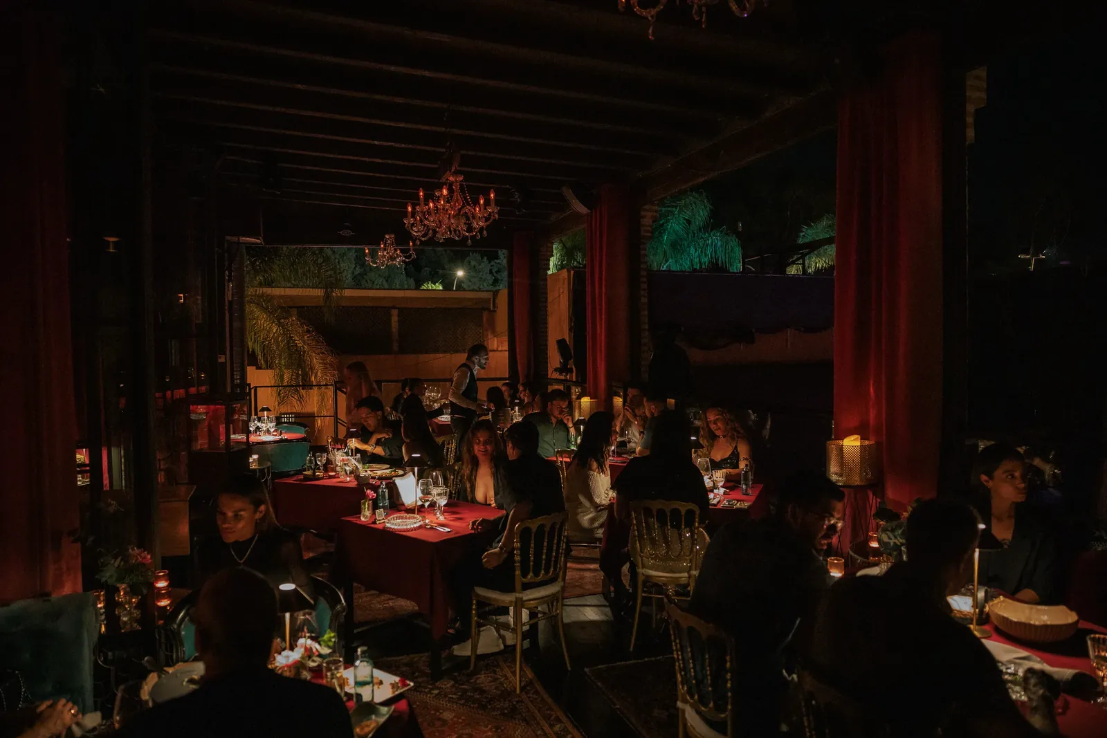 Salle de dîner tamisée de LØV Marbella aux rideaux rouges et tables dressées