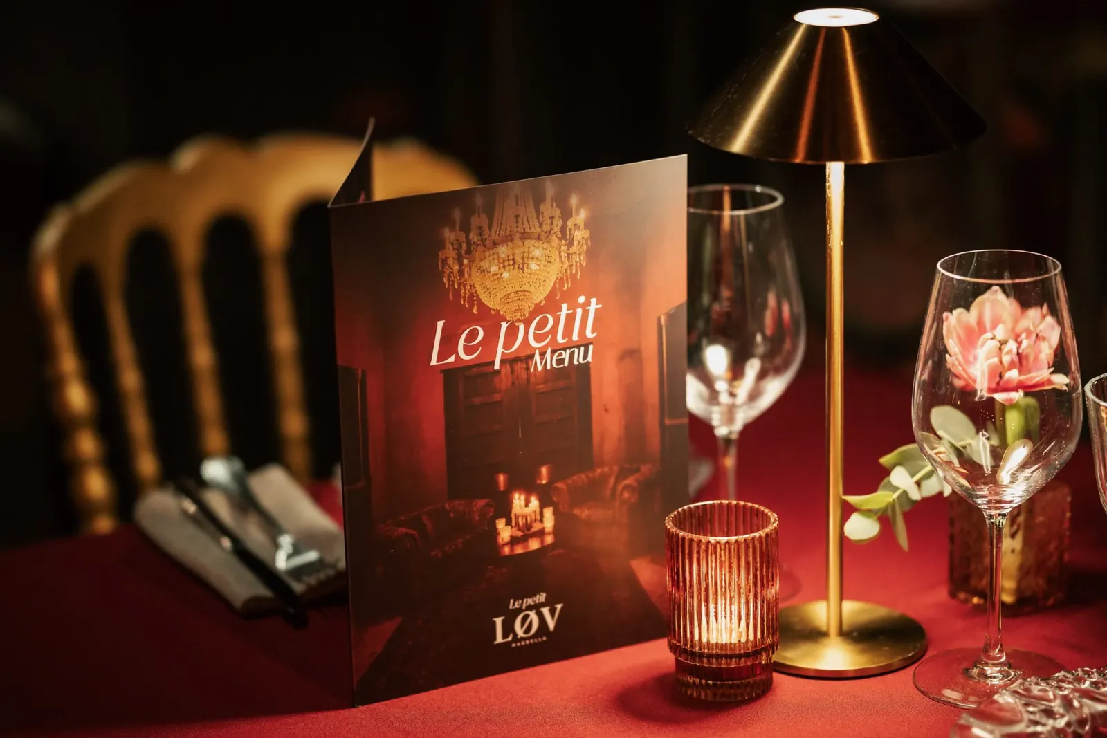 Menu et lampe dorée sur une table nappée de rouge à LØV Marbella