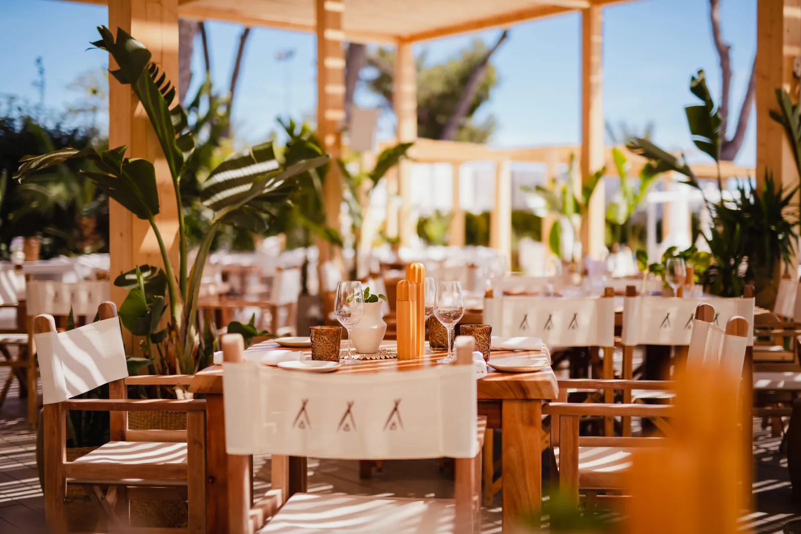 Tables set under pergolas at Nikki Beach Mallorca with tropical plants