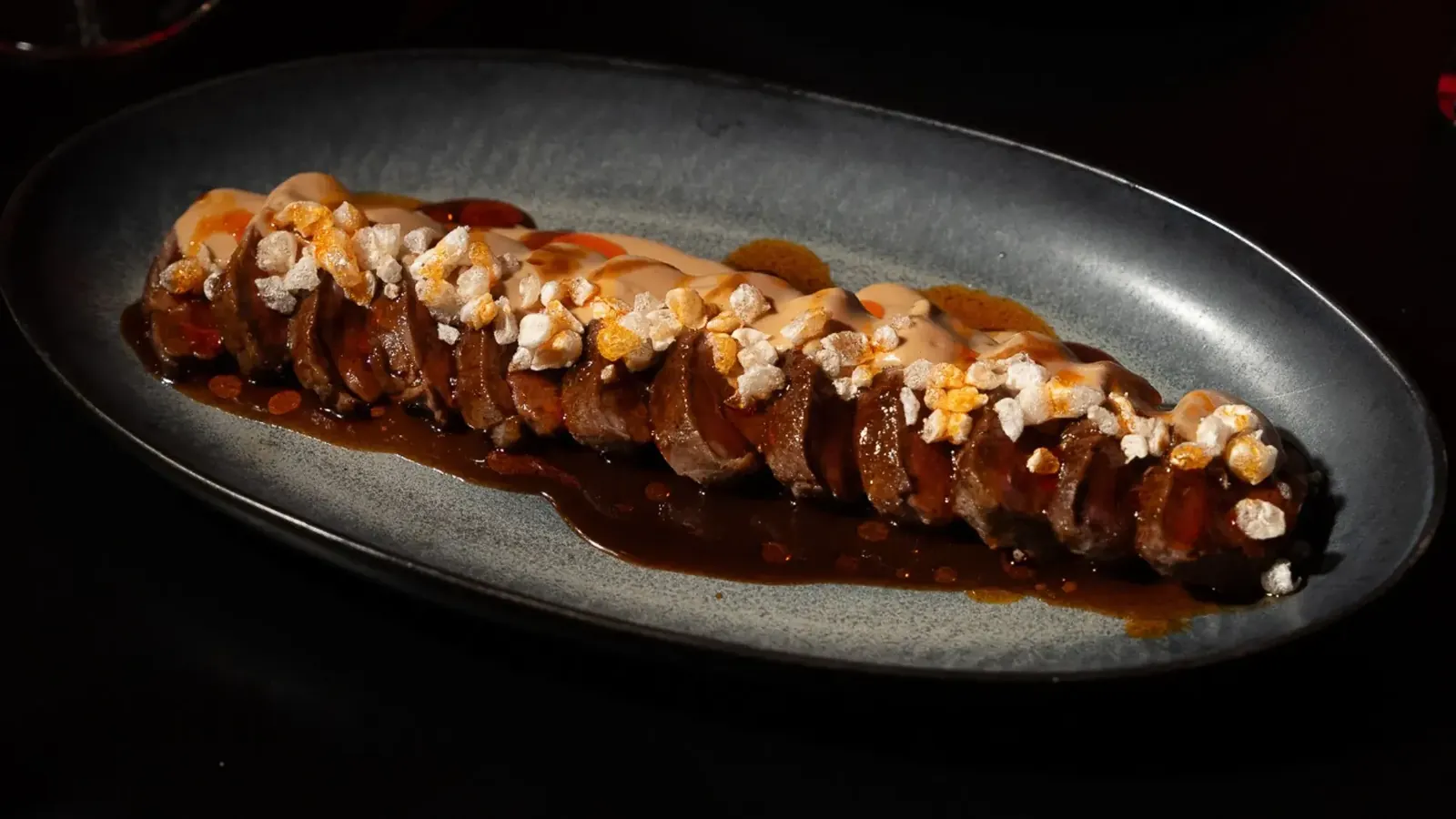 Sliced Iberian pork in brown sauce on dark plate at Pacha Ibiza