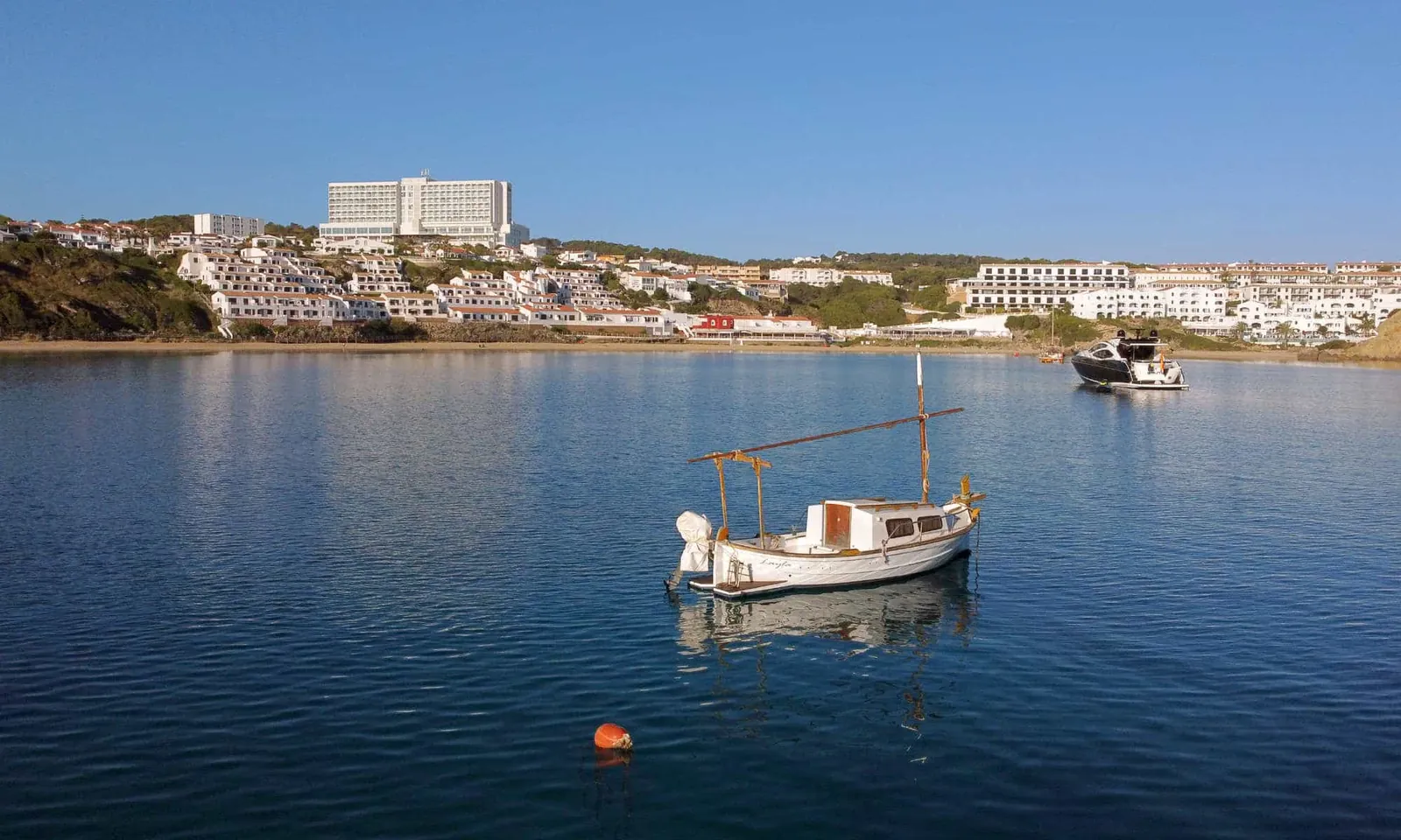 Bay of Arenal d'en Castell with a fishing boat and the hotel on the coast