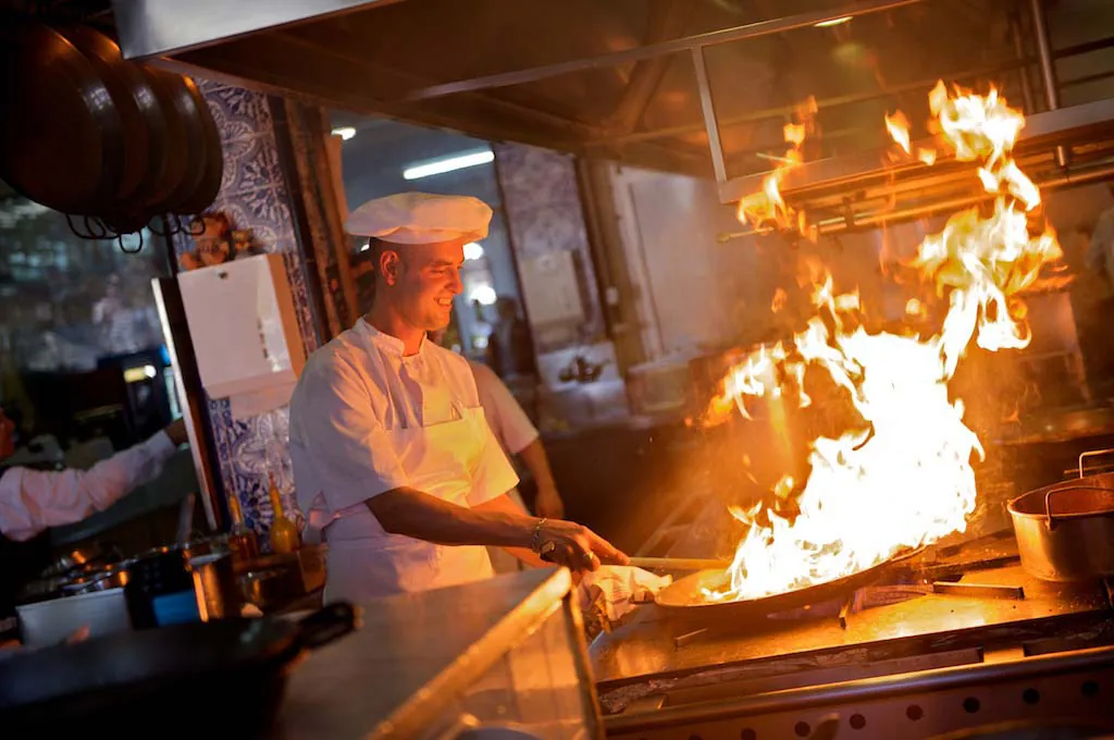 Chef flambéing a pan over fire in La Pepica kitchen in Valencia