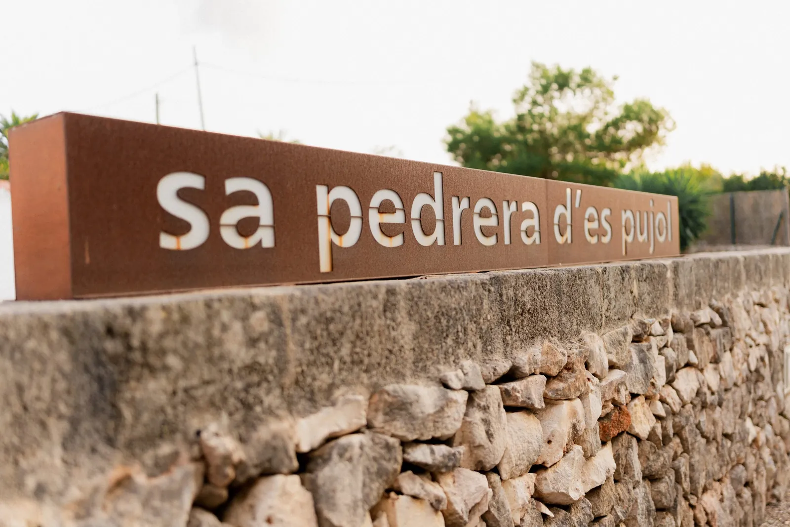 Metal sign reading sa pedrera d'es pujol on a stone wall in Sant Lluís